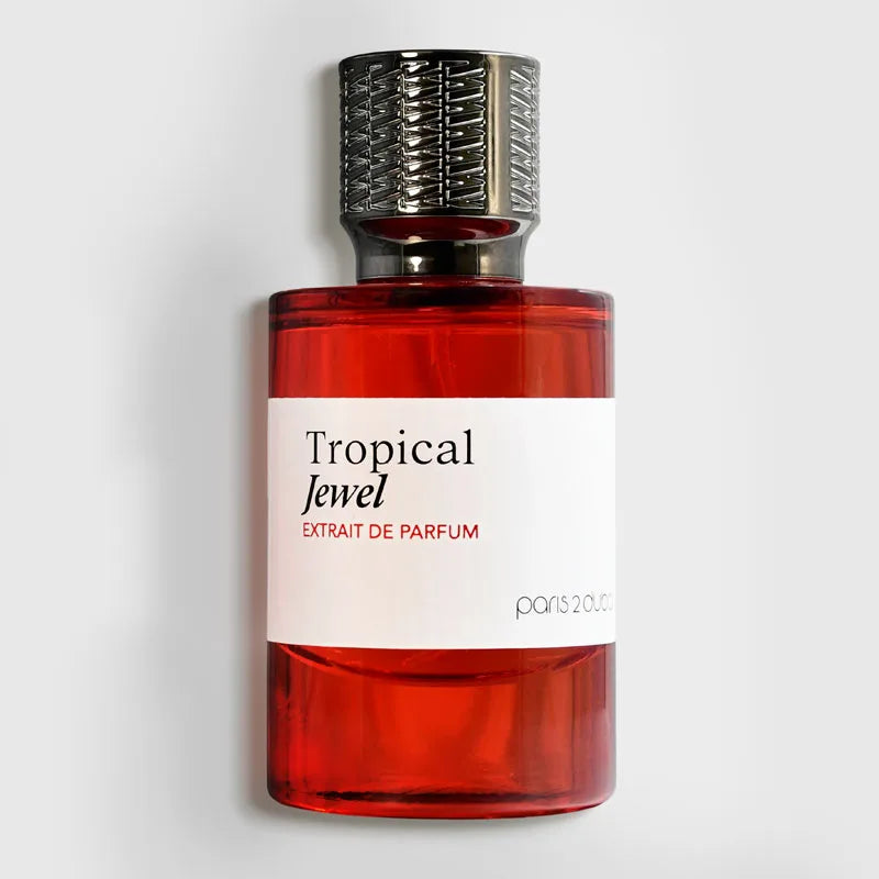 A bottle of Paris 2013 Tropical Jewel Extrait de Parfum with a translucent red glass body, a white label, and a textured metallic silver cap, set against a light gray background.