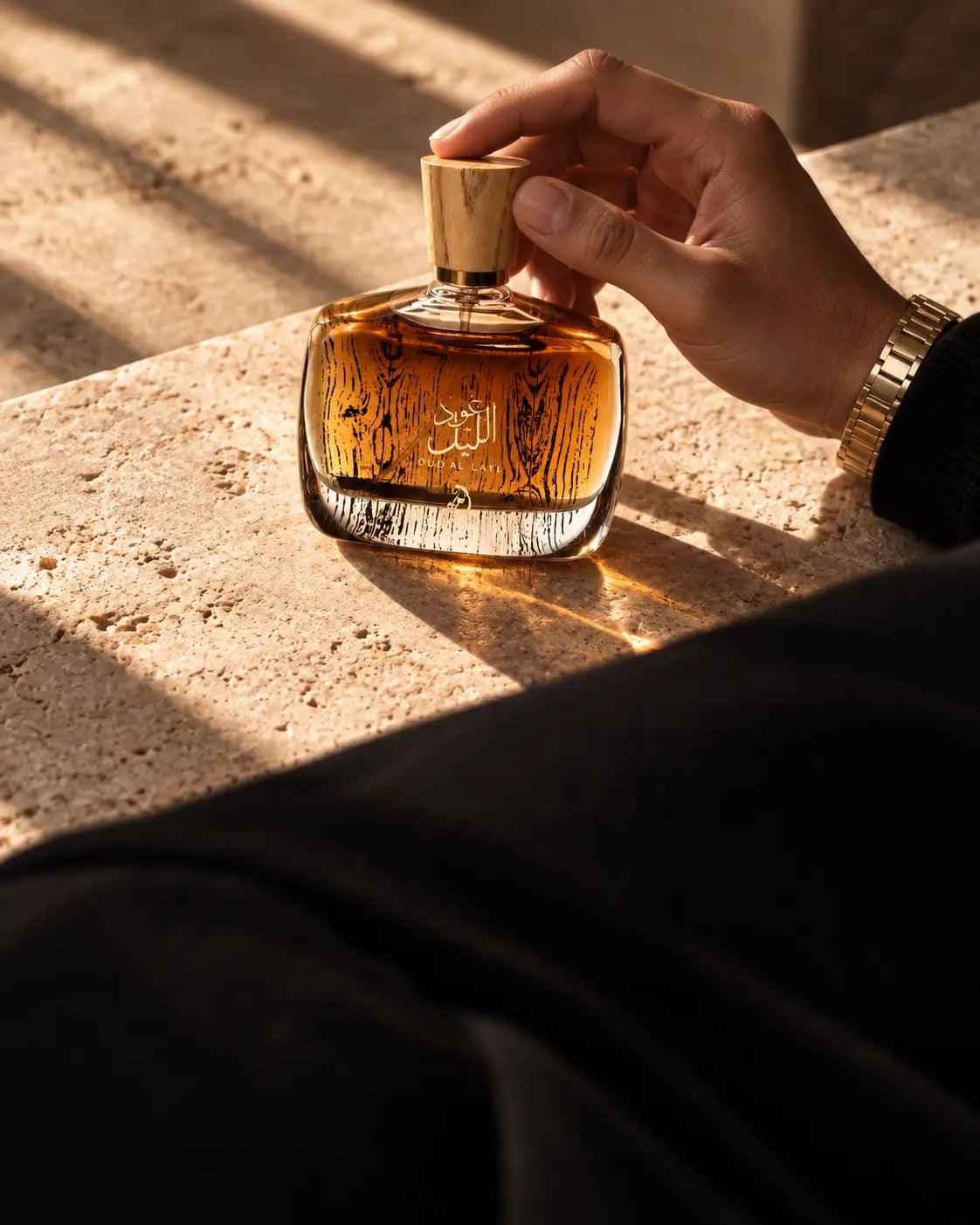 Oud Al Layl fragrance on travertine with a hand in warm sunlight