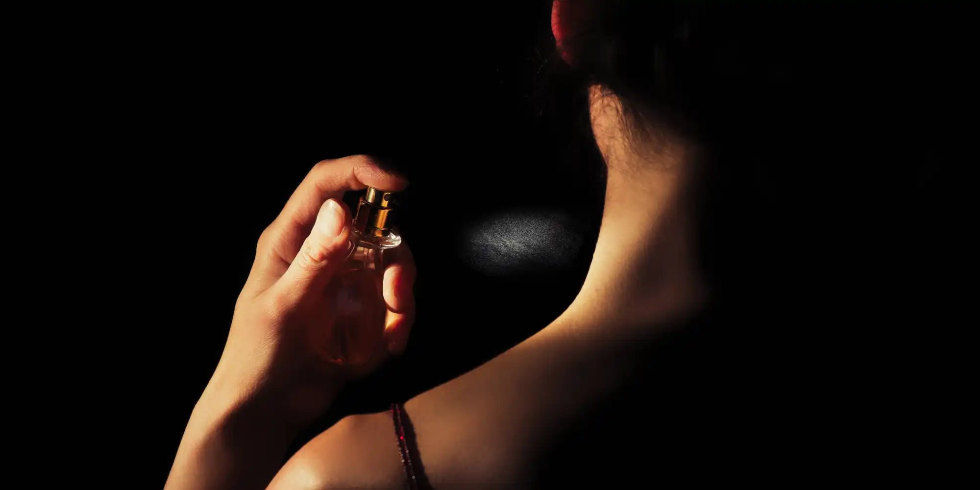 A hand spraying perfume in a dark setting.